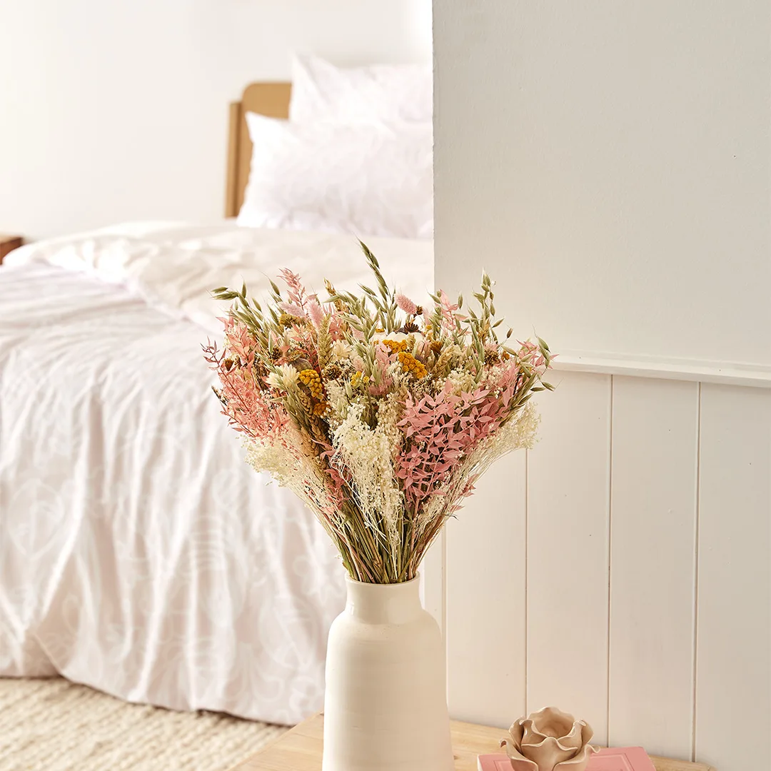 Vase de fleurs séchées devant un lit habillé du motif Flowrette.